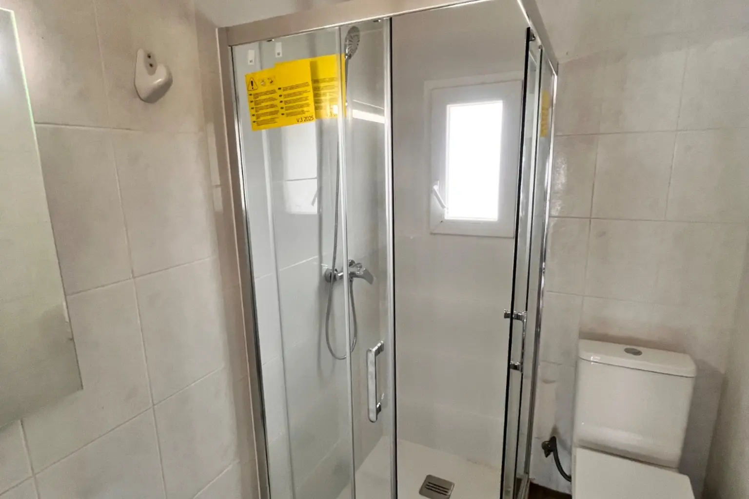 Mampara de ducha corredera de perfil cromado junto a la ventana del baño