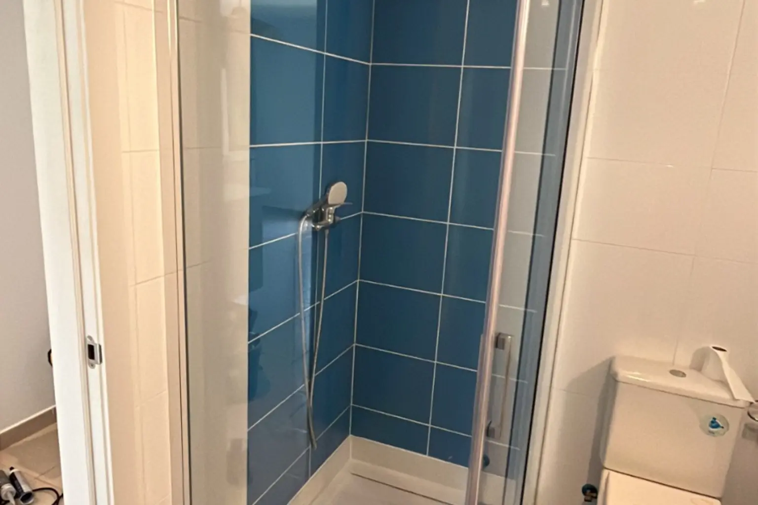 Mampara de ducha abatible de perfil cromado en un baño azul
