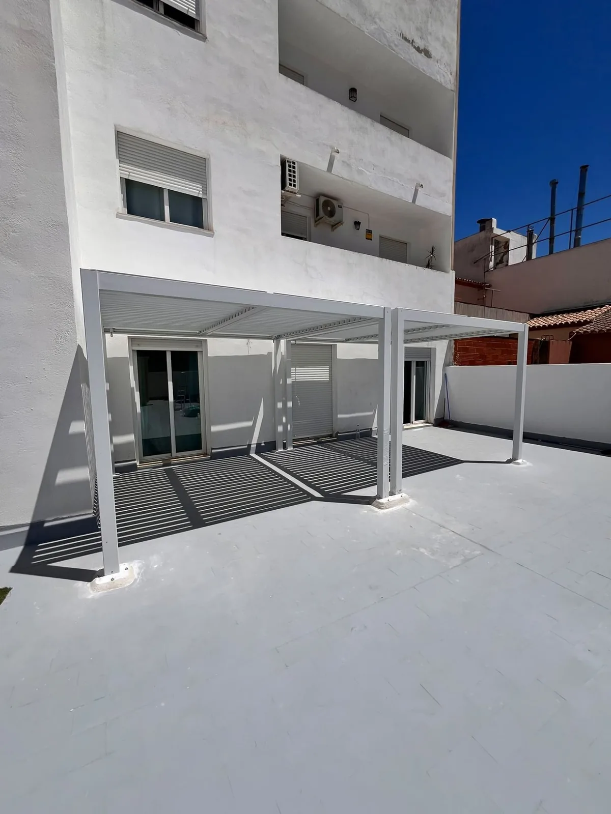 Aluminium bioclimatic pergola with the louvres angled, casting their shadow on the floor