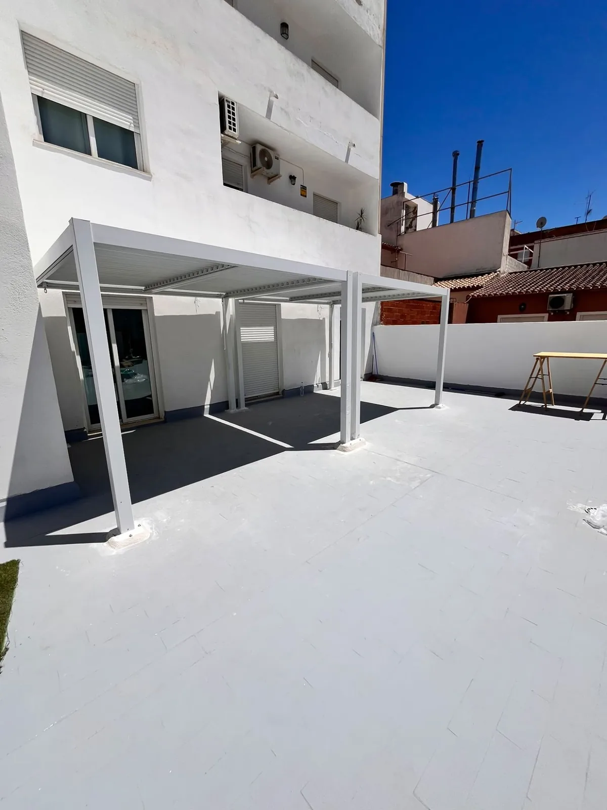 White bioclimatic pergola fitted on a terrace under a clear sky