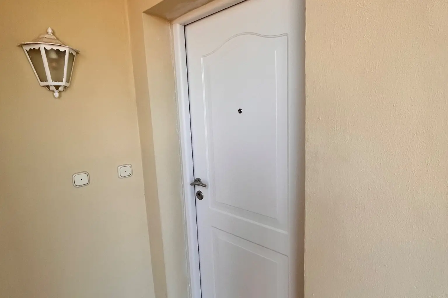 Puerta de entrada blanca instalada en un rellano con suelo de barro