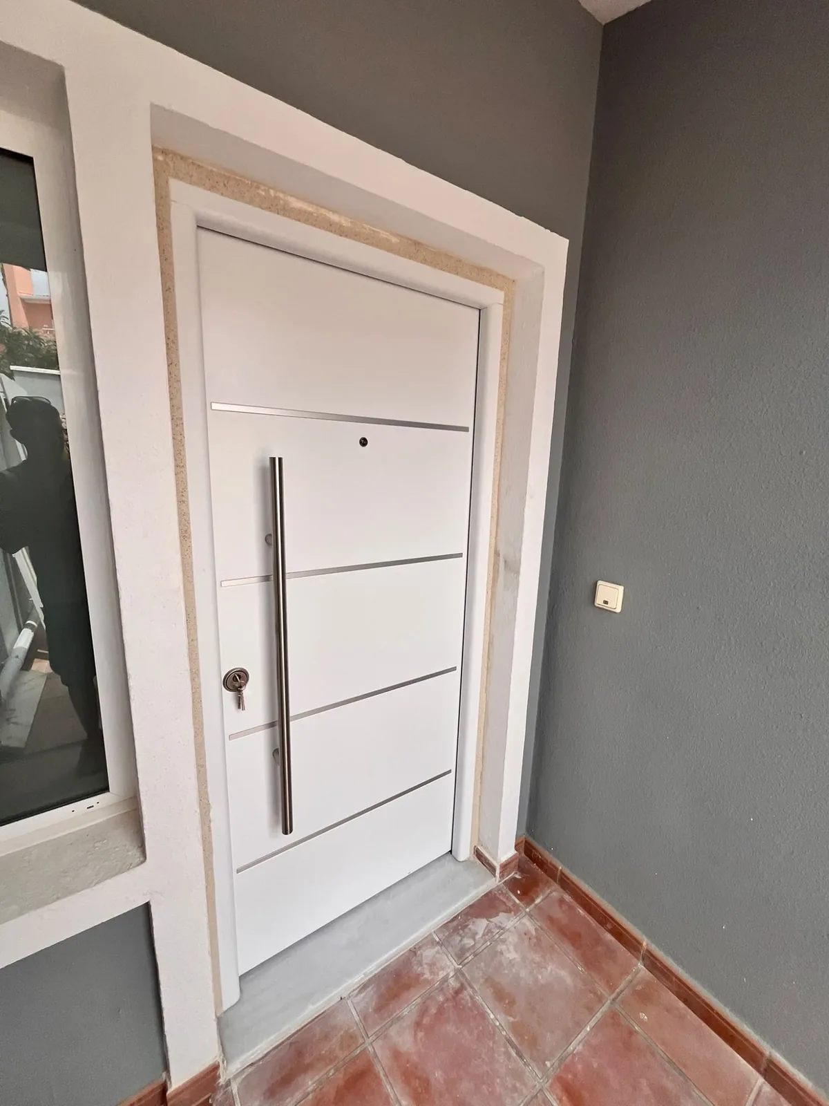 White front door with a vertical handle, seen at an angle from the landing